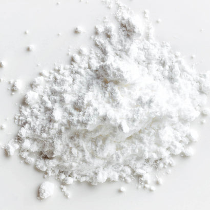 The image shows a close-up of a fine, white powder with a fluffy and soft texture. It appears clean and pure, spread over a smooth white surface, emphasizing its light, airy consistency.
